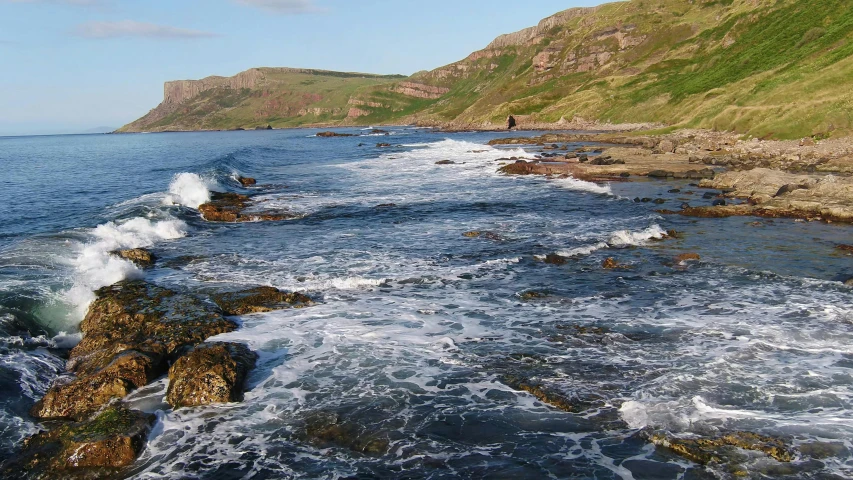 a large body of water next to a lush green hillside, an album cover, by Alison Watt, pexels, les nabis, rocky seashore, marsden, currents, university