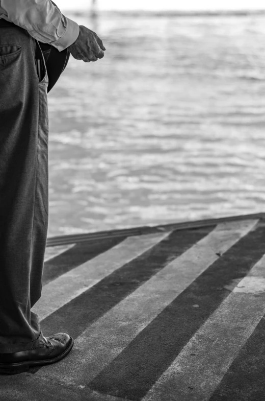 a man standing next to a body of water, a black and white photo, inspired by Louis Stettner, unsplash, detail, on the deck of a ship, folded, wearing a tracksuit