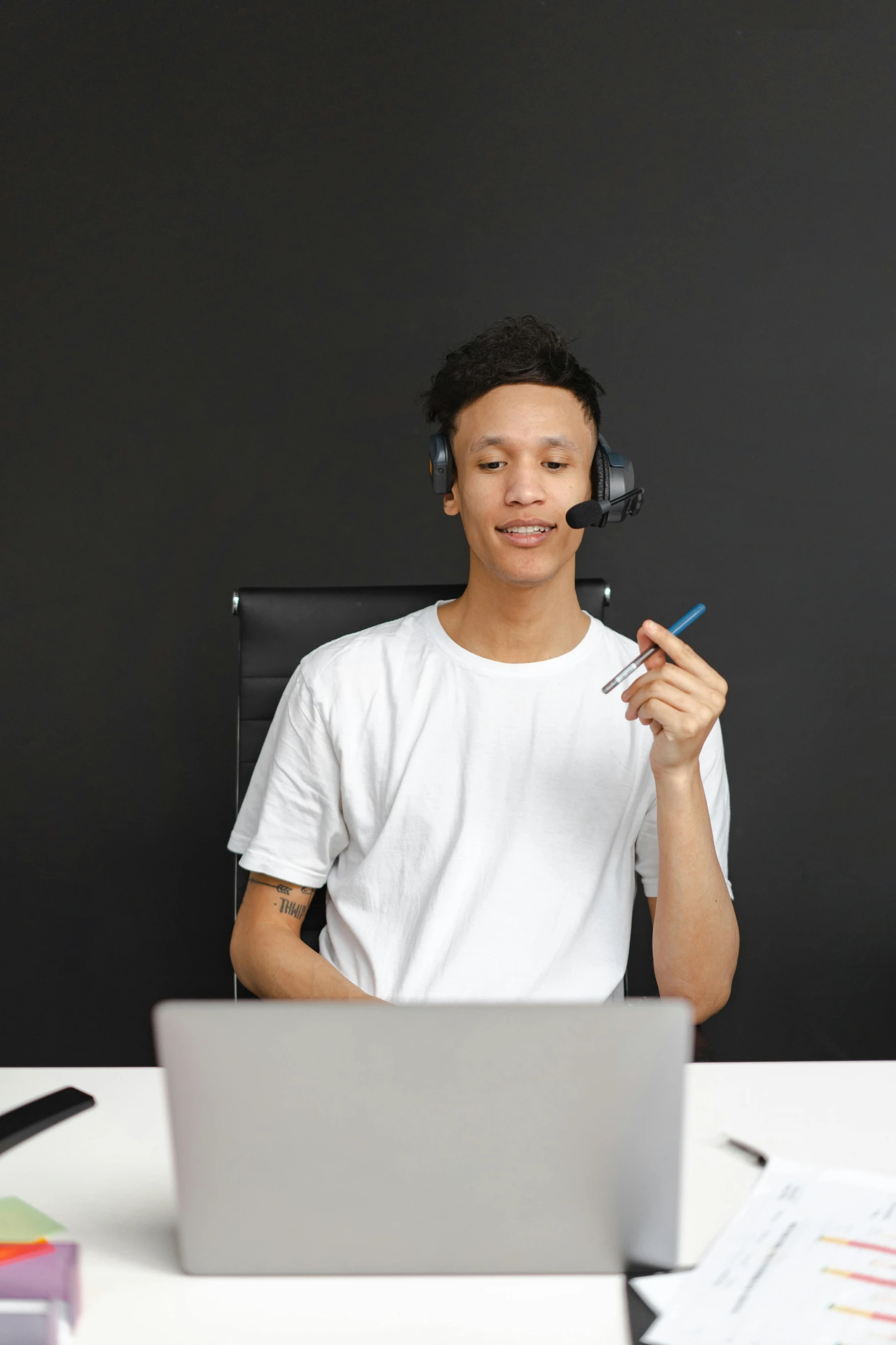 a man sitting at a desk with a laptop and headphones, a computer rendering, trending on pexels, renaissance, holding microphone, black teenage boy, an all white human, standing with a black background