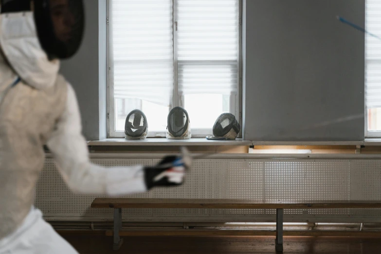 a fencer in a fencing stance in front of a window, an abstract sculpture, inspired by Wilhelm Hammershøi, pexels contest winner, kinetic art, sitting in a waiting room, partially masked, on a white table, in a classroom