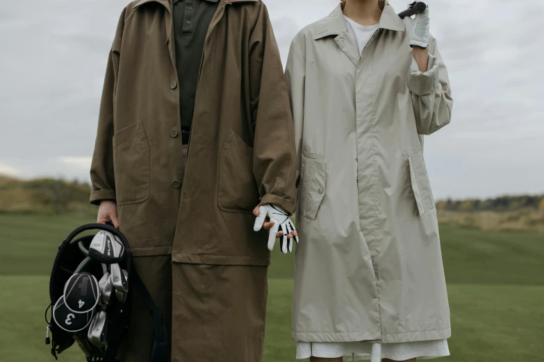 a man and a woman standing next to each other, unsplash, renaissance, trench coat, golf course, brown, worn