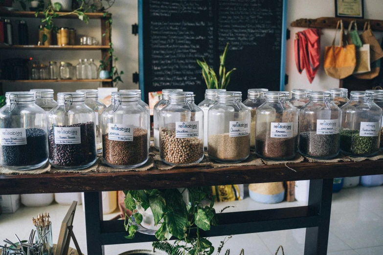 a bunch of jars sitting on top of a wooden table, by Julia Pishtar, trending on unsplash, inside a french cafe, abundant fruition seeds, jar on a shelf, gravels around