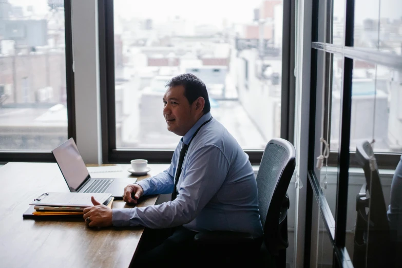 a man sitting at a desk in front of a laptop computer, inspired by Eddie Mendoza, unsplash, hurufiyya, in an call centre office, te pae, long street, next to window