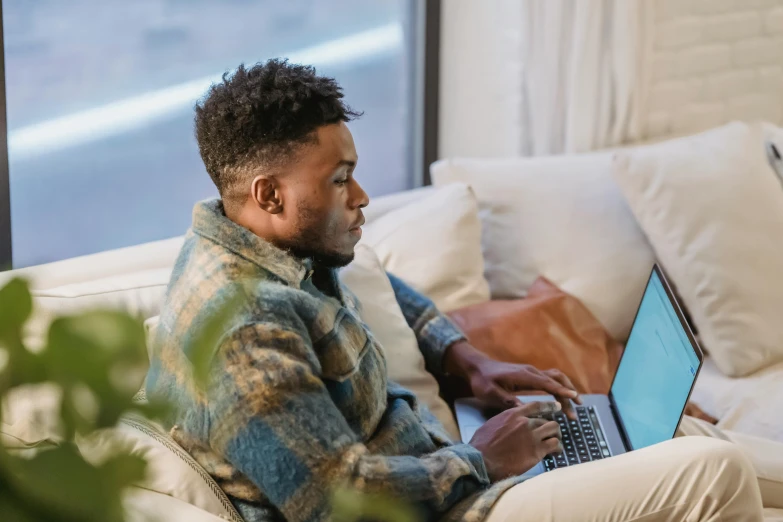 a man sitting on a couch using a laptop, trending on pexels, jaylen brown, facing sideways, avatar image, thumbnail