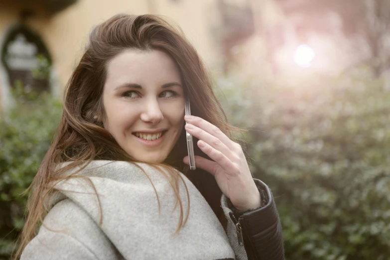 a woman holding a cell phone to her ear, by John Murdoch, trending on pexels, attractive brown hair woman, winter sun, friendly smile, medium format. soft light