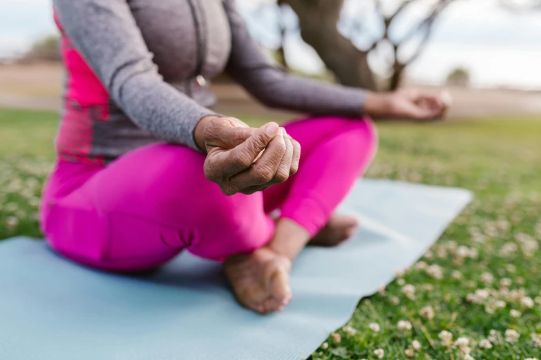 a woman sitting on a yoga mat in the grass, pexels, spinning hands and feet, focus on the foreground, manuka, wrinkles and muscle tissues