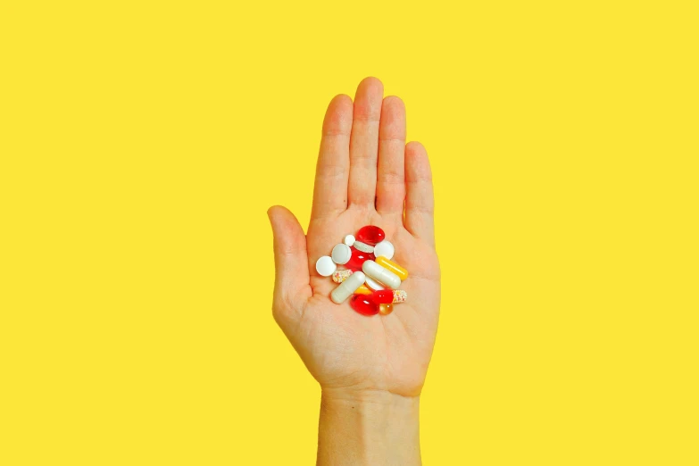 a person holding a bunch of pills in their hand, by Julia Pishtar, yellow and red, raised hand, ultra definition, medium