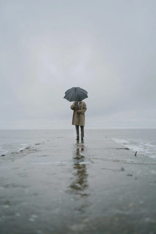 a person standing in the water with an umbrella, by Jesper Knudsen, looking melancholy, shoreline, standing in road, gray men