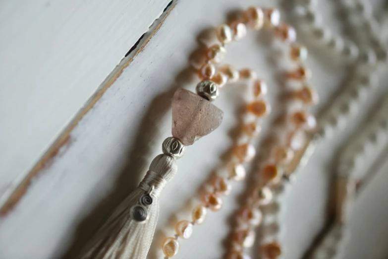 a close up of a beaded necklace with a tassel, inspired by Perle Fine, unsplash, renaissance, rose quartz, pearl, rustic, closeup photograph