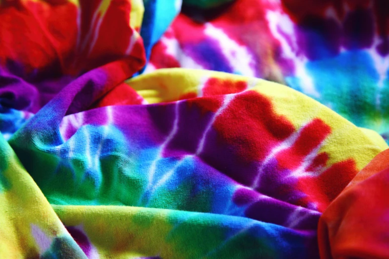 a colorful tie dye blanket laying on top of a bed, inspired by Gabriel Dawe, unsplash, process art, colorful bandana, psychedelic art style, bright trouser suit for a rave, upclose