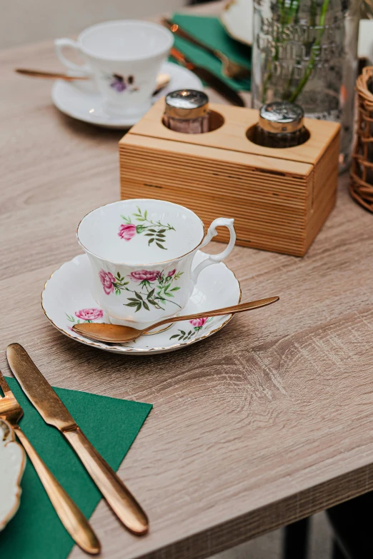 a wooden table topped with plates and silverware, tea cup, pink and green colour palette, premium, carrington