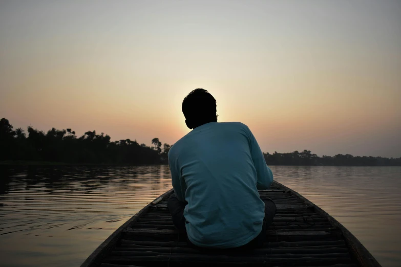 a man sitting on the edge of a boat at sunset, pexels contest winner, hurufiyya, assamese aesthetic, depressed, grey, backfacing