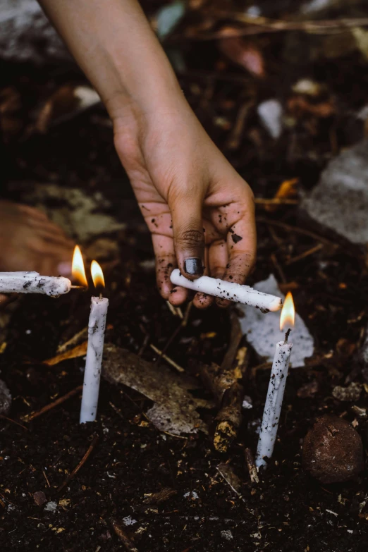 a person lighting candles in the dirt, inspired by Elsa Bleda, unsplash, land art, smoking a joint, white candles, trash, ignant