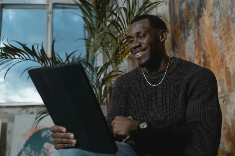 a man sitting in front of a laptop computer, pexels contest winner, brown skin man with a giant grin, black man, he is wearing a brown sweater, thumbnail