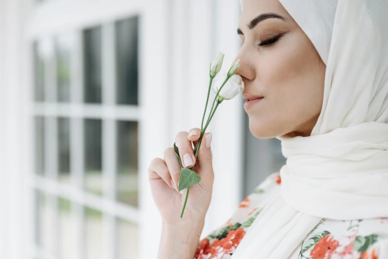 a woman wearing a hijab smelling a flower, inspired by Maryam Hashemi, trending on pexels, hurufiyya, wearing white silk, femalev beauty, looking from side, middle eastern details