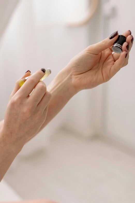 a woman applying her nails in front of a mirror, by Gavin Hamilton, pexels, floating in perfume, on grey background, vibrant vials, finger blend shading