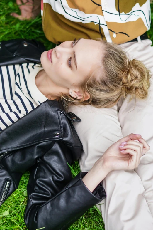 a woman laying on top of a lush green field, inspired by Elsa Bleda, trending on pexels, wearing leather jacket, someone sits in bed, close up of a blonde woman, hair styled in a bun