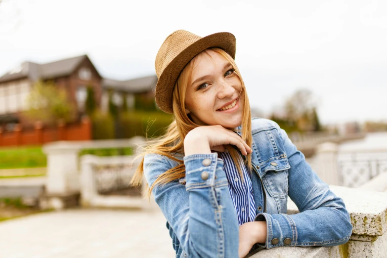 a woman in a hat leaning on a wall, trending on pexels, happening, relaxing and smiling at camera, avatar image, nice weather, wearing a jeans jackets