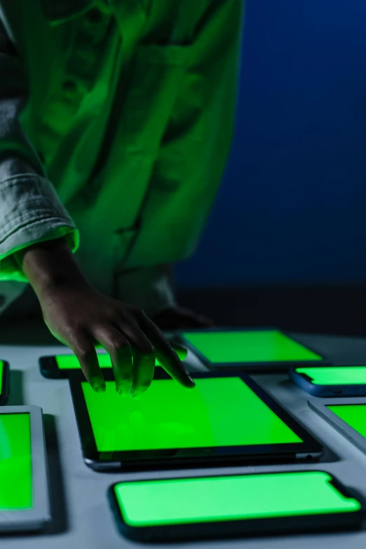 a person touching a green screen on a table, a silk screen, inspired by Bruce Nauman, trending on unsplash, interactive art, softly glowing control panels, inside of a 1970s science lab, using a magical tablet, backlighted