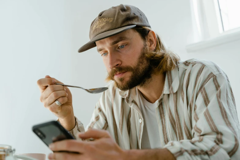 a man sitting at a table with a spoon and a cell phone, trending on pexels, hyperrealism, scruffy brown beard, caracter with brown hat, blonde guy, mukbang