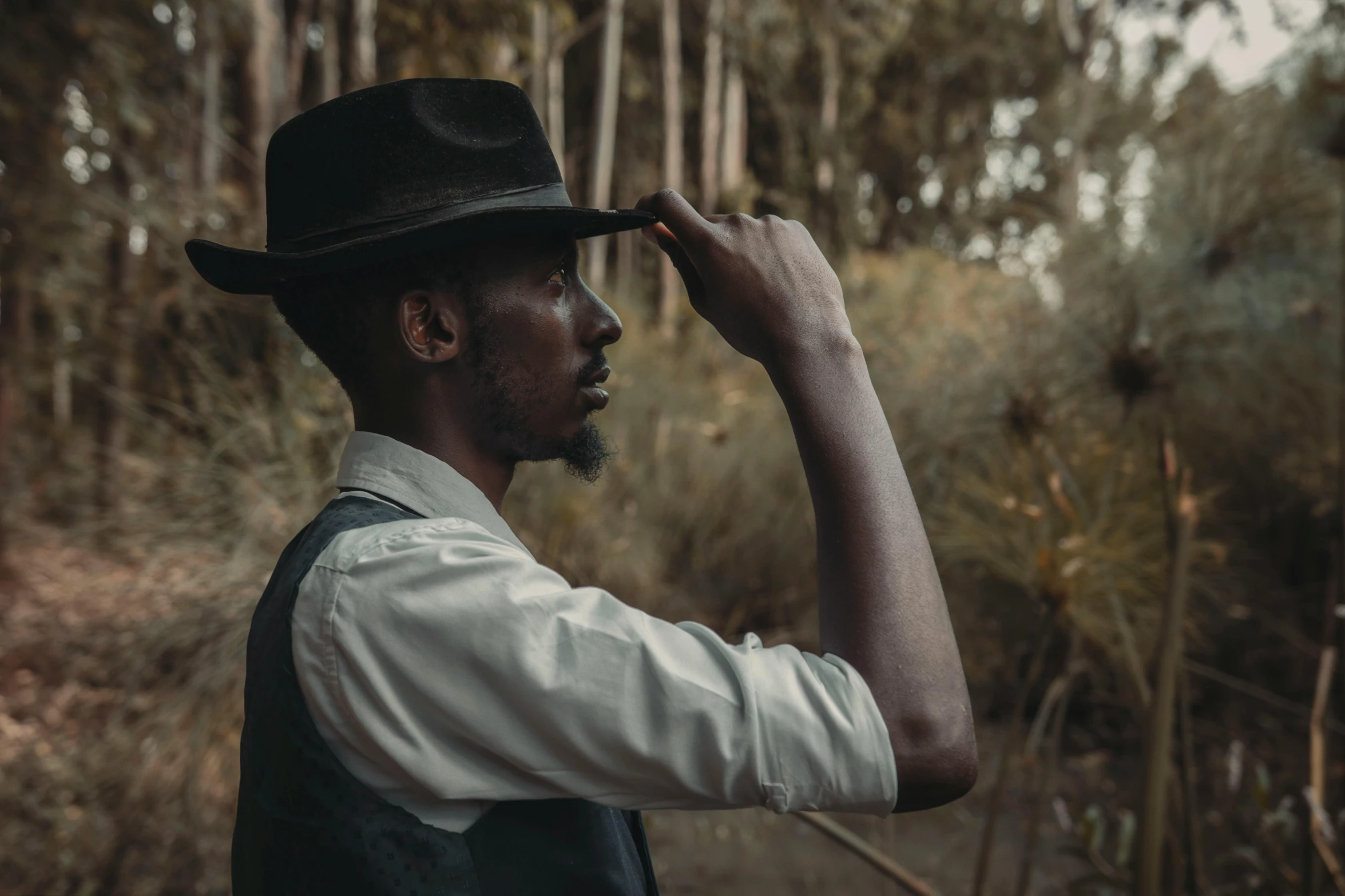 a man in a hat standing in a forest, an album cover, pexels contest winner, australian tonalism, african man, profile pose, half african, looking into the horizon