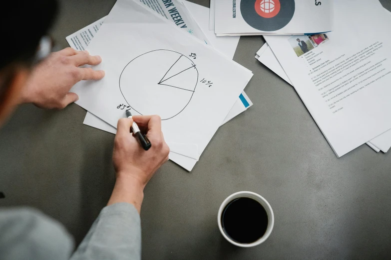 a person sitting at a table with papers and a pen, proportions on a circle, promo image, whiteboards, multiple stories