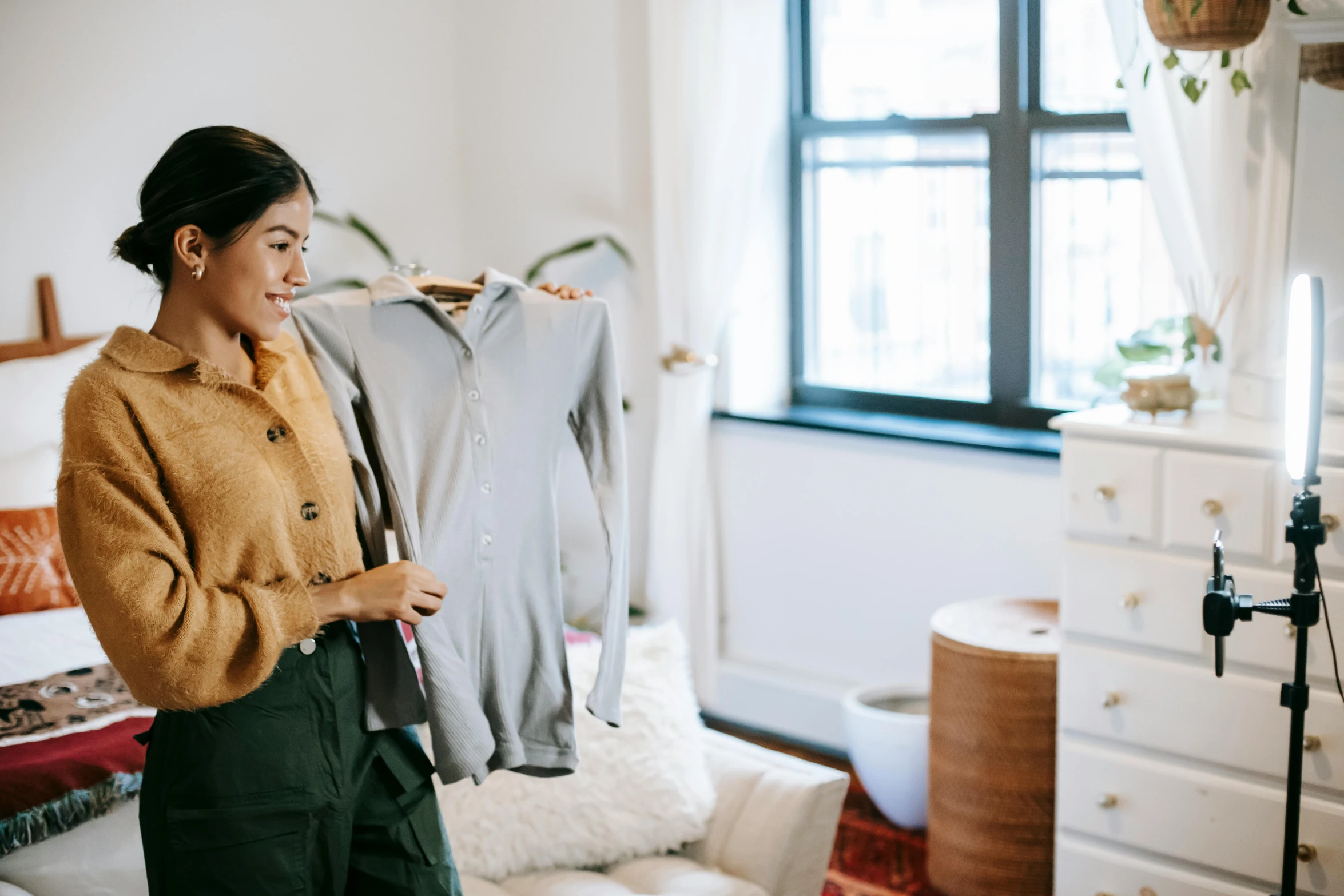 a woman standing in front of a bed holding a jacket, pexels contest winner, happening, inspect in inventory image, 🦩🪐🐞👩🏻🦳, office clothes, wearing a green sweater