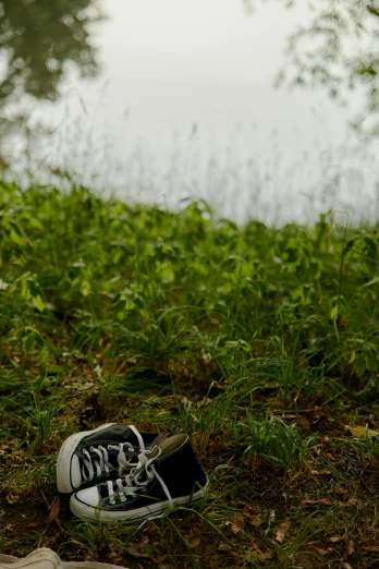 a pair of shoes sitting on the ground next to a body of water, in the grass, on a green hill between trees, cinematic shot ar 9:16 -n 6 -g, photograph