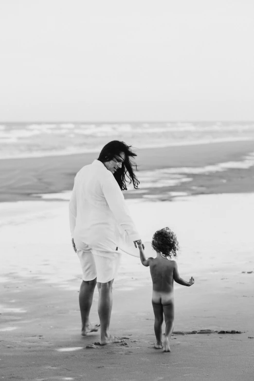 a black and white photo of a woman and a child on the beach, a black and white photo, ariel perez, walking on water, instagram post, man