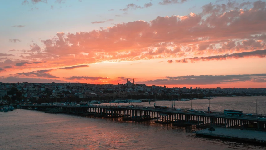 a bridge over a body of water with a sunset in the background, pexels contest winner, hurufiyya, turkish and russian, city in background, pink clouds in the sky, youtube thumbnail