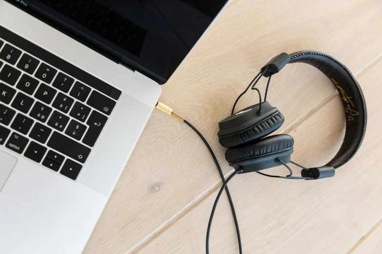 a laptop computer sitting on top of a wooden table, an album cover, pexels, wearing black headphones, black and gold wires, thumbnail, programming