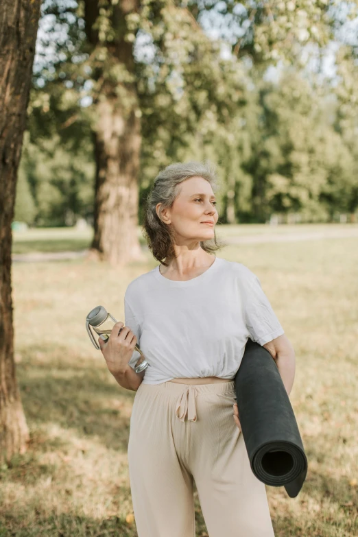 a woman holding a yoga mat in a park, by Matija Jama, pexels contest winner, happening, portrait 6 0 - year - old woman, 15081959 21121991 01012000 4k, holding arms on holsters, profile picture