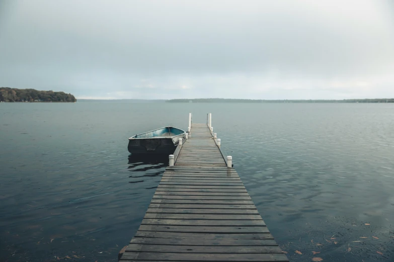 a boat sitting on top of a wooden dock, by Jaakko Mattila, pexels contest winner, minimalism, overcast lake, low quality footage, shades of blue and grey, fading off into the distance