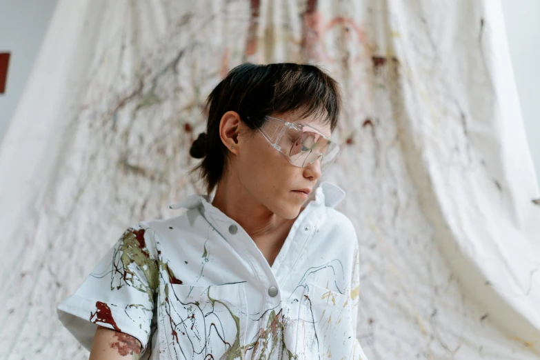 a woman standing in front of a white curtain, inspired by Shōzō Shimamoto, trending on pexels, gutai group, goggles on forehead, painted overalls, boy with neutral face, marbling