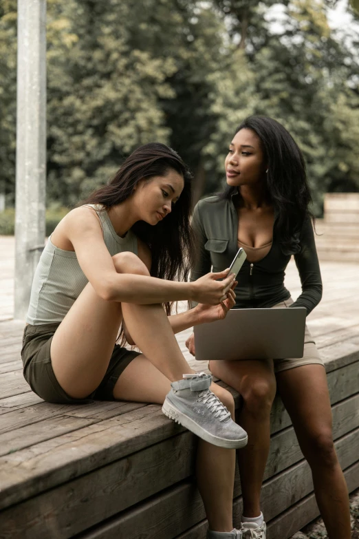 two women sitting on a bench looking at a laptop, trending on pexels, sexy girl wearing shorts, green and brown clothes, phone, 2 techwear women