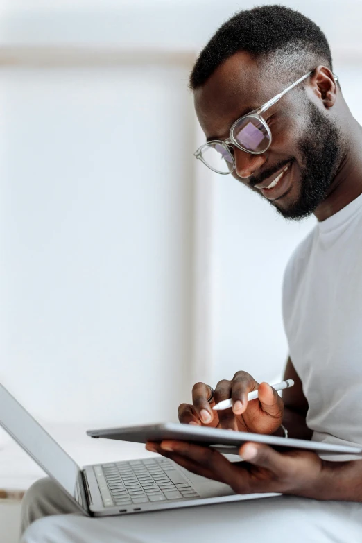 a man sitting on a couch using a laptop, trending on pexels, brown skin man with a giant grin, white reading glasses, using a magical tablet, dynamic closeup