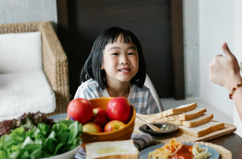 a little girl sitting at a table with a plate of food, inspired by Yukimasa Ida, pexels contest winner, healthy, eating garlic bread, kids talking to fruit people, beautiful asian girl