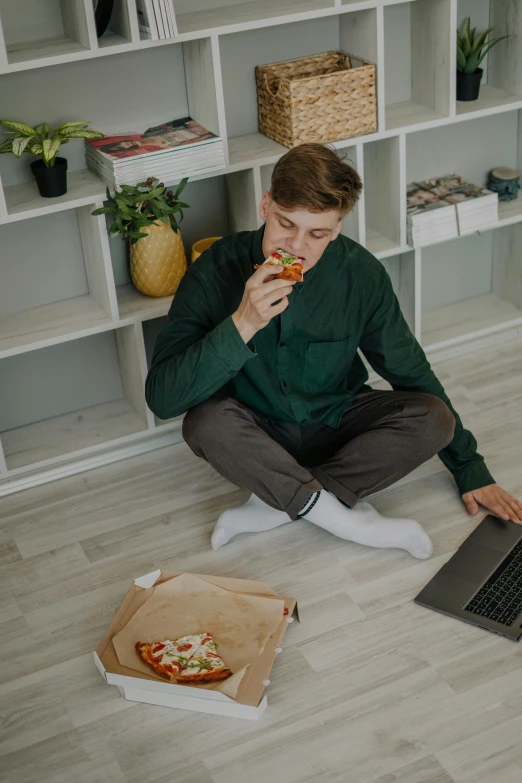 a man sitting on the floor eating a slice of pizza, wearing business casual dress, everything fits on the screen