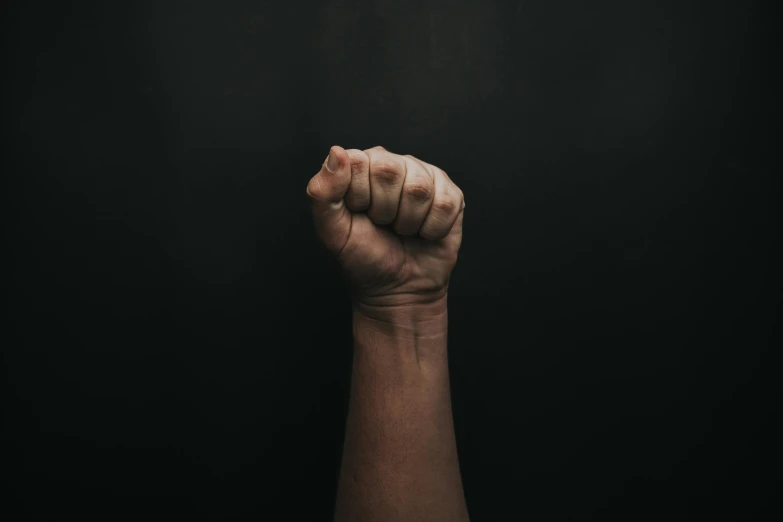 a clenched hand against a black background, pexels contest winner, raised fist, with brown skin, background image, instagram post