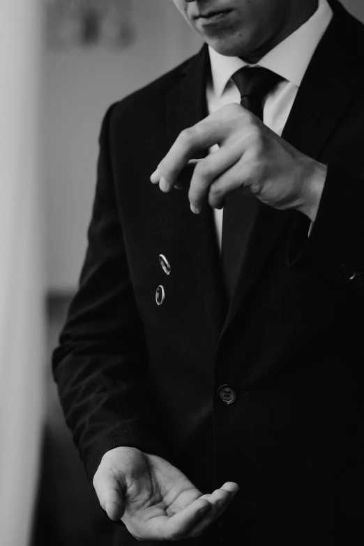 a man in a suit adjusting his tie, a black and white photo, by Emma Andijewska, unsplash, badge on collar, album cover, wearing black modern clothes, point finger with ring on it