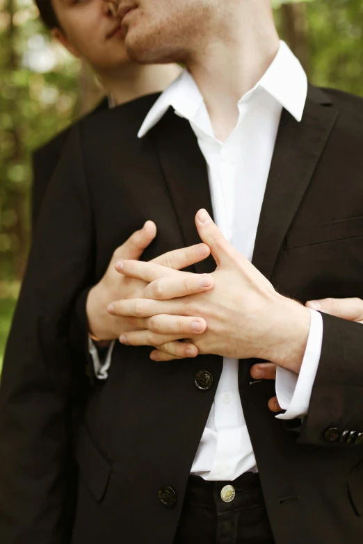 a couple of men standing next to each other, an album cover, by Julia Pishtar, unsplash, renaissance, subject detail: wearing a suit, heart, hands crossed, heavy gesture style closeup