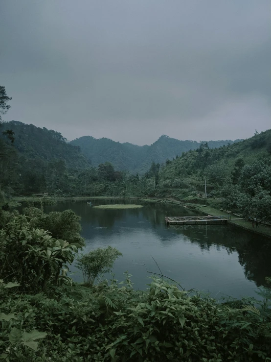 a river running through a lush green forest, inspired by Elsa Bleda, sumatraism, overcast lake, trending on vsco, hills in the background, nostalgic melancholy