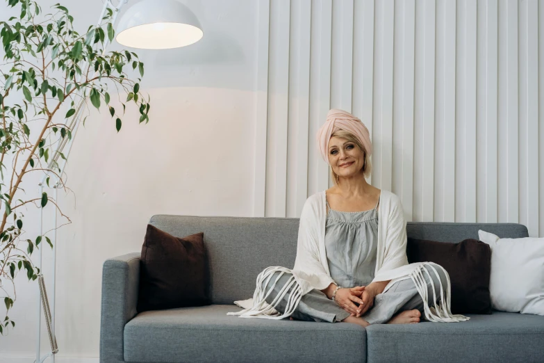 a woman sitting on a couch in a living room, a portrait, inspired by Joanna Carrington, pexels contest winner, turban, haruno sakura, scandinavian style, slight overcast lighting