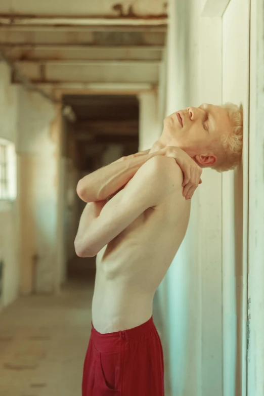 a man in red shorts leaning against a wall, an album cover, unsplash, renaissance, intense albino, bare chest, dancer, pastel'