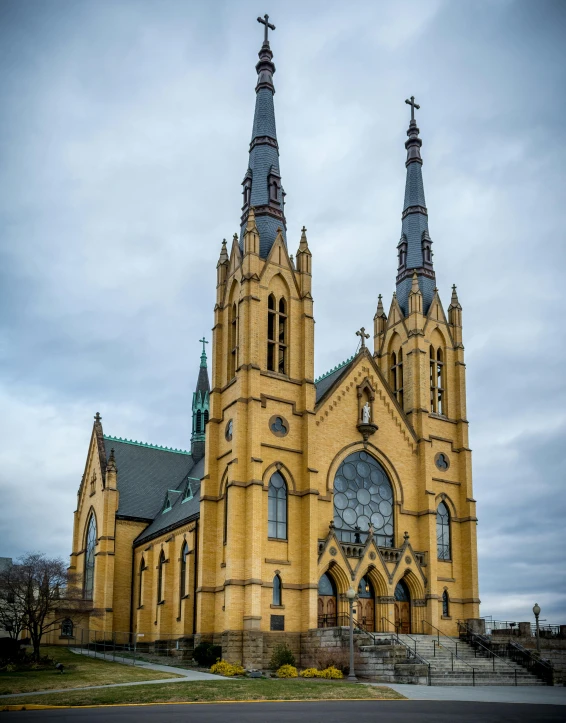 a large yellow church sitting on top of a lush green field, a photo, by Jacob Burck, pexels contest winner, art nouveau, majestic spires, on a cloudy day, marilyn church h, lgbtq