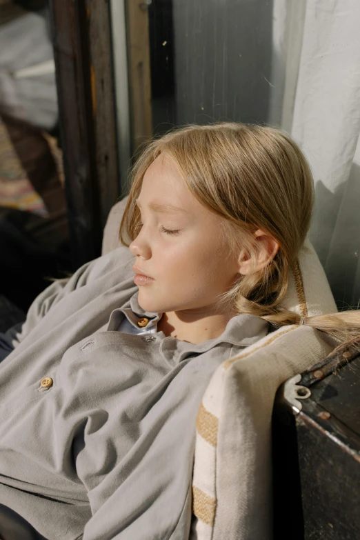 a little girl laying on top of a bed next to a suitcase, an album cover, by Sigrid Hjertén, pexels, wearing a grey robe, deep in thought, movie scene close up, in a comfortable chair