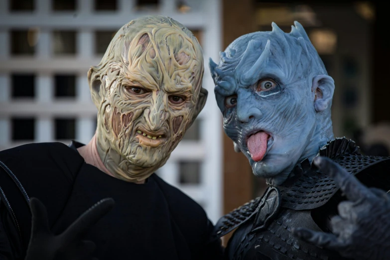 a couple of men standing next to each other, prosthetic makeup, with blue skin, scary creatures in background, from of thrones