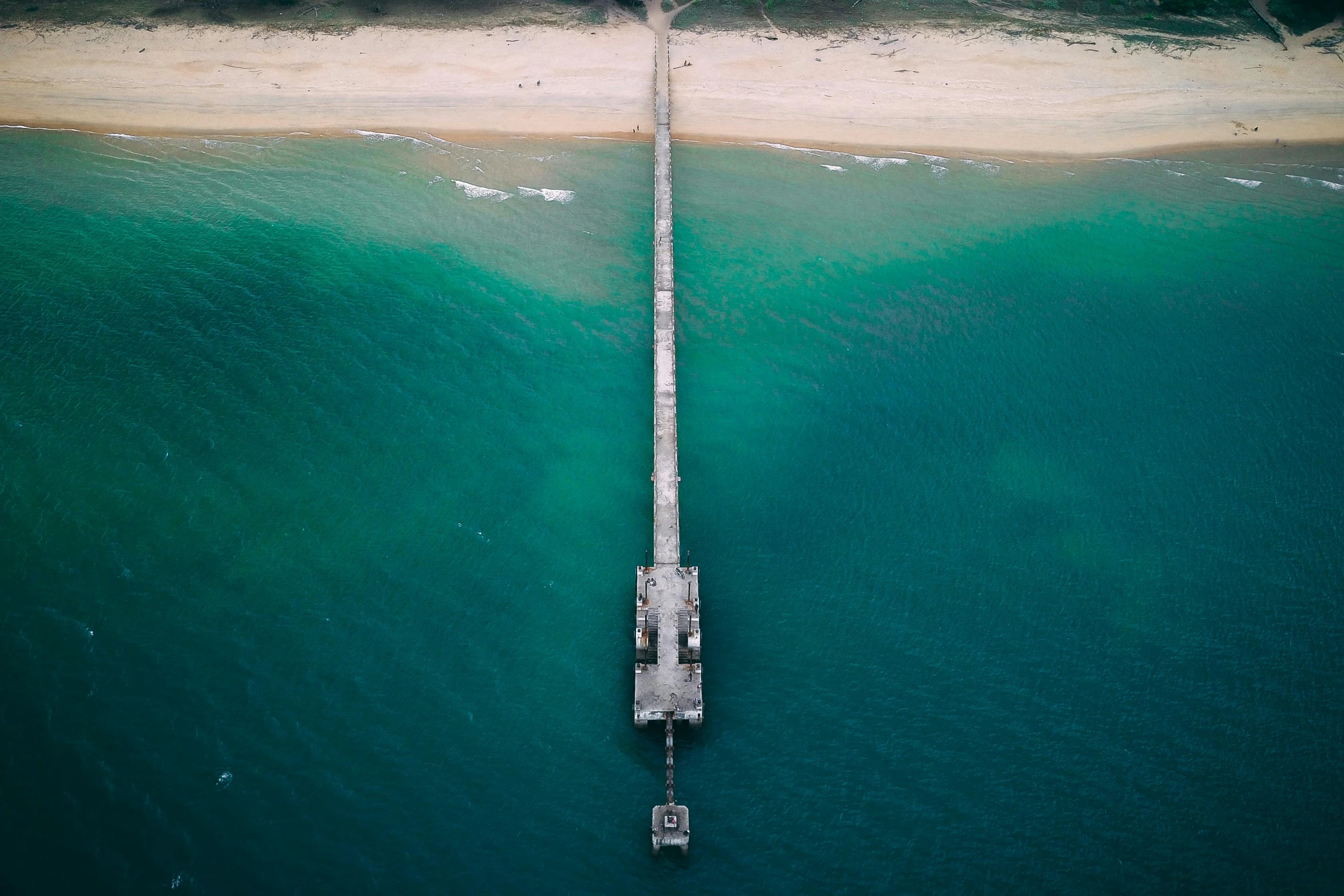 a long pier in the middle of a body of water, by Peter Churcher, unsplash contest winner, hurufiyya, helicopter view, gold coast australia, greenish blue tones, nazare (portugal)