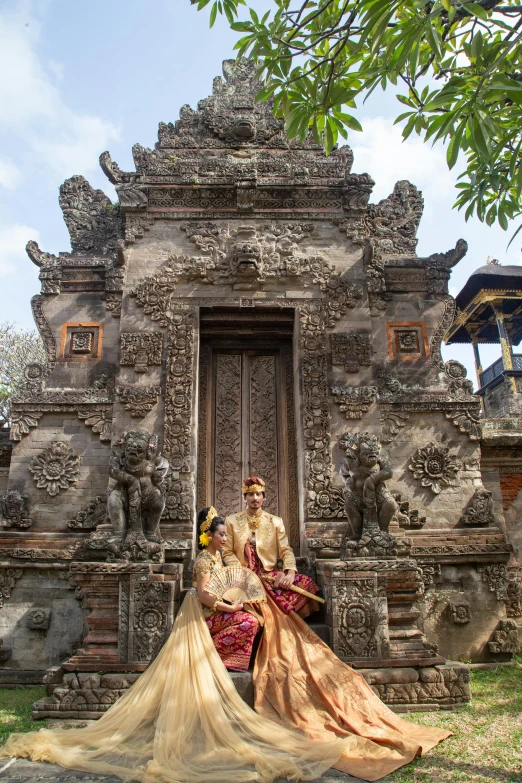 a man and a woman sitting in front of a building, a statue, inspired by I Ketut Soki, renaissance, perched on intricate throne, wedding, full front view, grotto