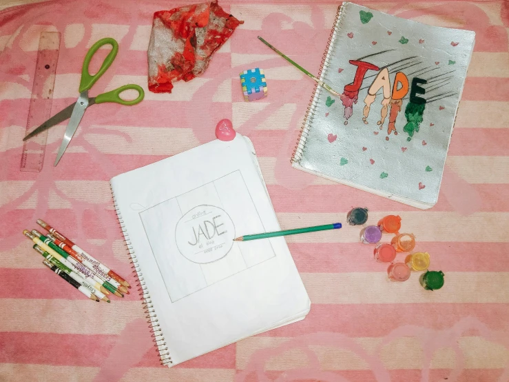 a book sitting on top of a bed next to a pair of scissors, a child's drawing, inspired by JoWOnder, process art, pink and red color scheme, jade, schematic in a notebook, coloring page